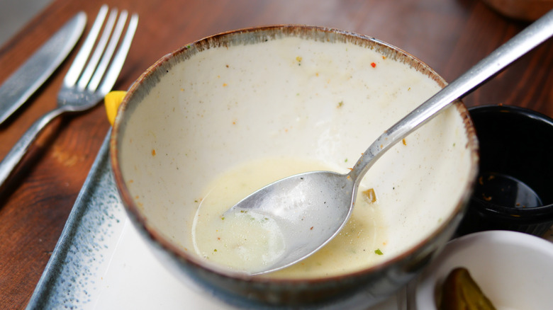A ceramic bowl with a spoon and remnants of soup