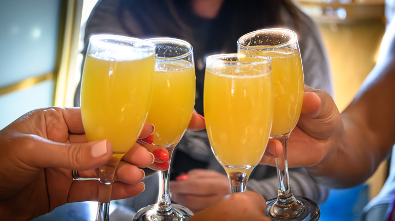 Close up of four friends clinking champagne flutes filled with orange colored mimosas.