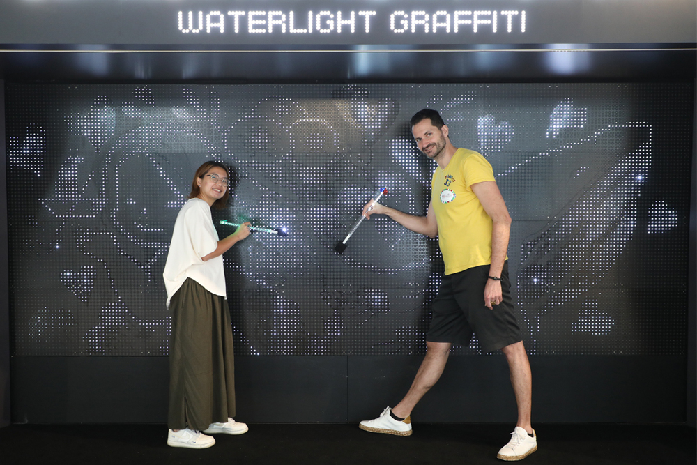 Hong Kong-based artist Bao Ho creates artworks on the captivating interactive Waterlight Graffiti installation by French artist Antonin Fourneau, exemplifying cross-cultural exchange through art.