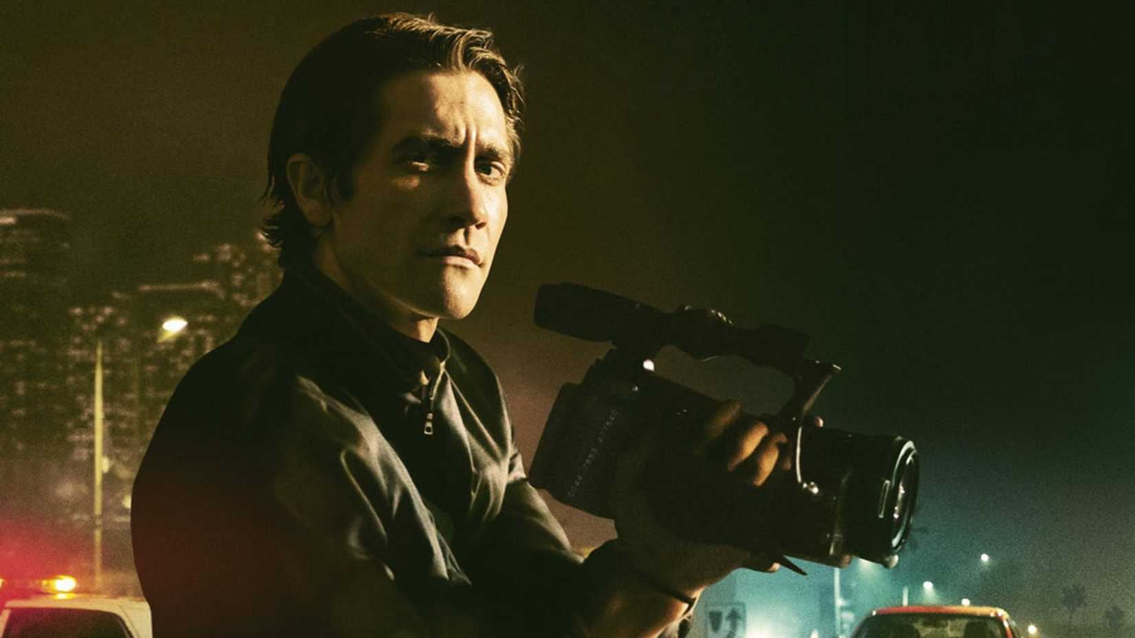 Jake Gyllenhaal holds a camera against the backdrop of the city in Nightcrawler.