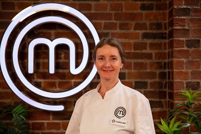 A woman in her chef whites (Caroline) poses in the MasterChef studios. 