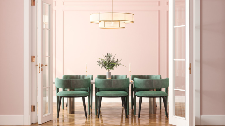 A modern dining room with pastel pink walls and green chairs