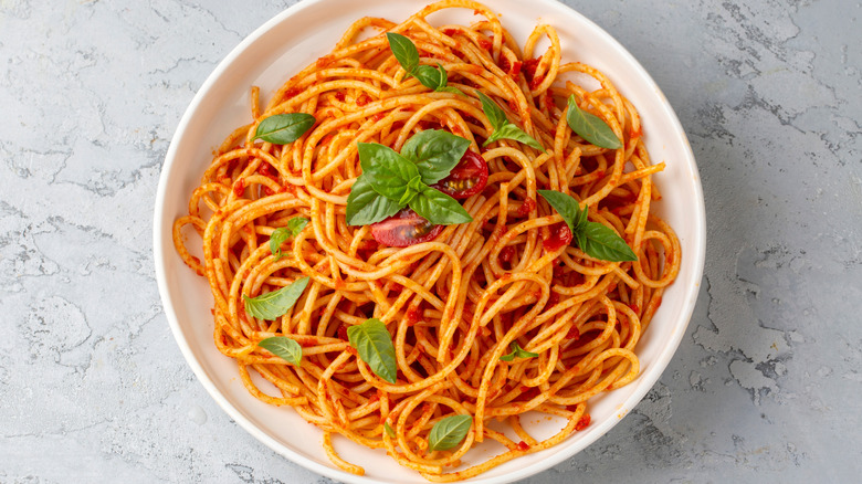 A plate of pasta with red grape tomatoes and green basil leaves on a gray stone counter background.