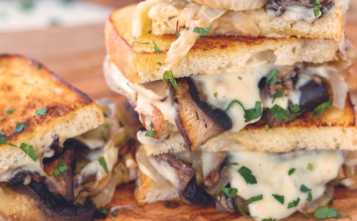 a fried portobello mushroom and spicy vegan cheese sauce sandwich with caramelized onions