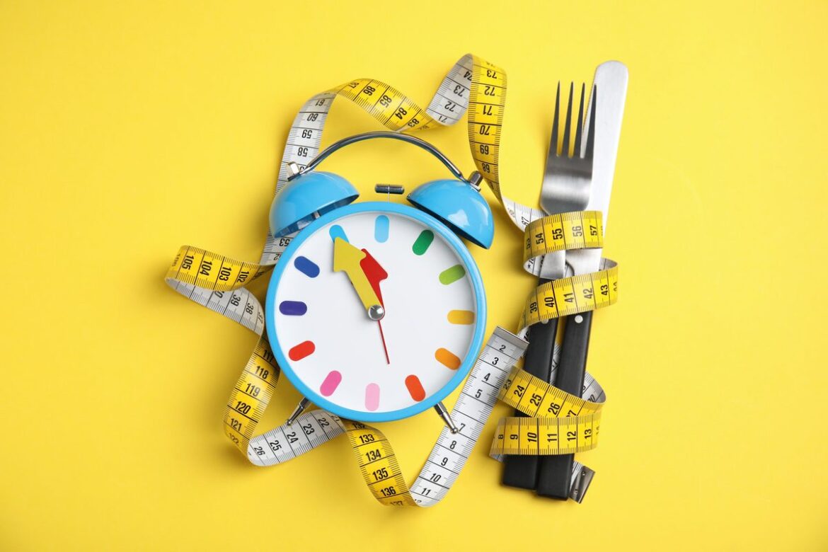 Alarm clock, measuring tape and cutlery on yellow background, flat lay