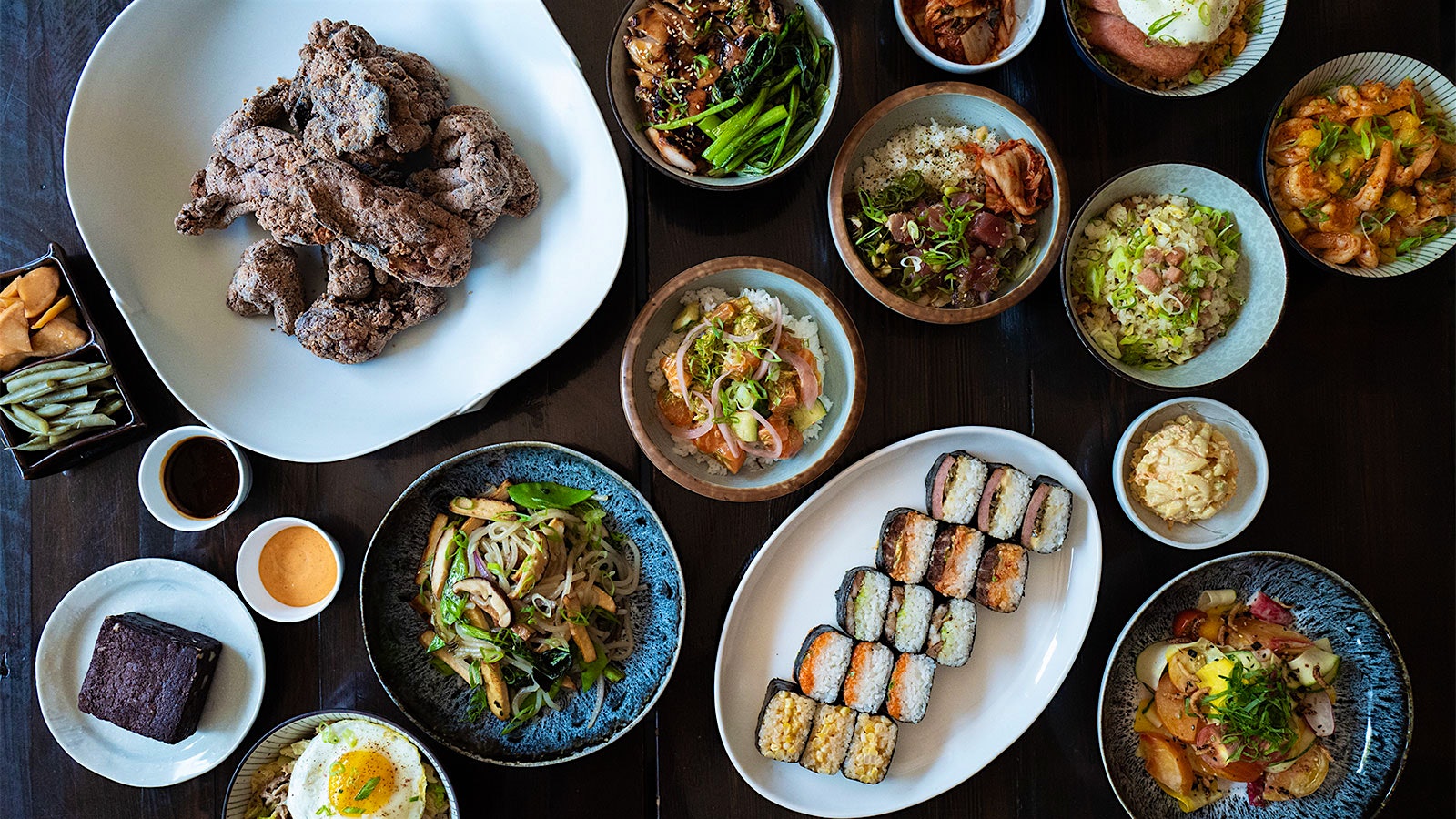  Spam musubi, fried chicken, noodles, a fried egg and other dishes on a table at Noreetuh