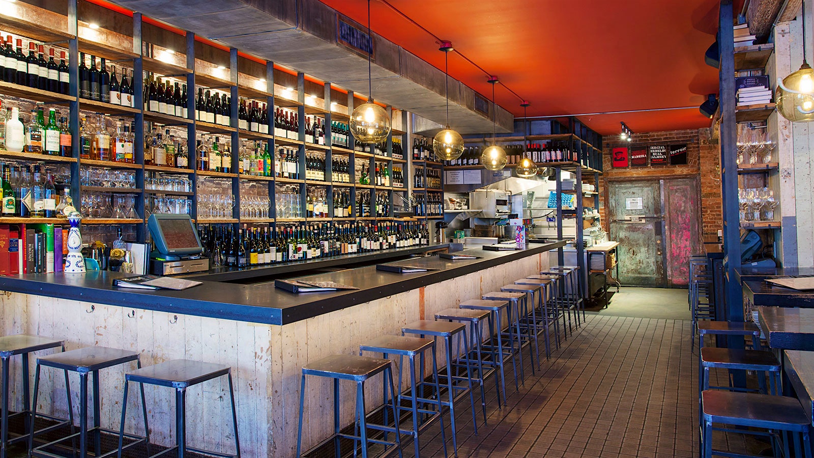  The gray bar at Terroir in Tribeca, with an orange ceiling, metal stools shelves of wine and spirits bottles