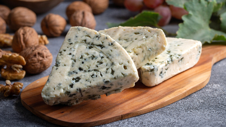 Wedges of Roquefort on a wooden board with nuts in the background