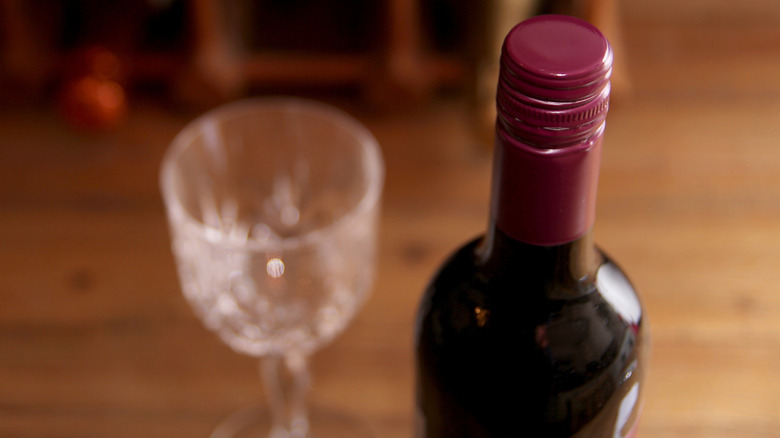 Screw-top red wine next to a textured wine glass on wood