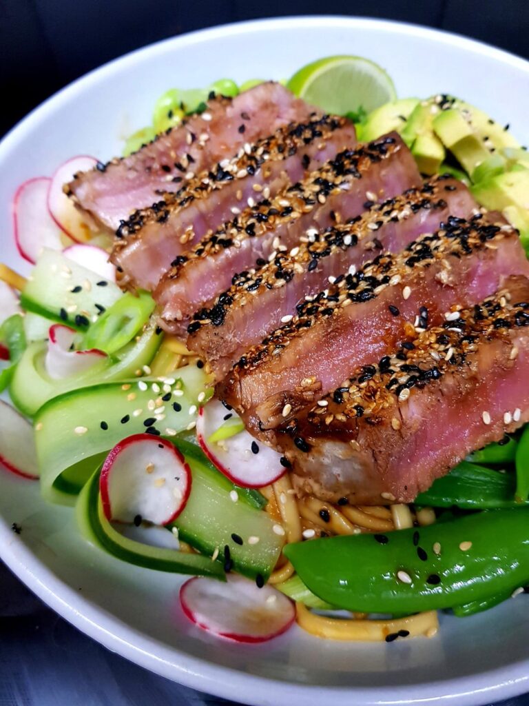 Sesame Crusted Tuna Steak with (Hidden) Saucy Udon Noodles. Pickled Cucumber and Radish, Snap Peas, Edamame, Avocado and Herbs. Plus Extra Seeds.