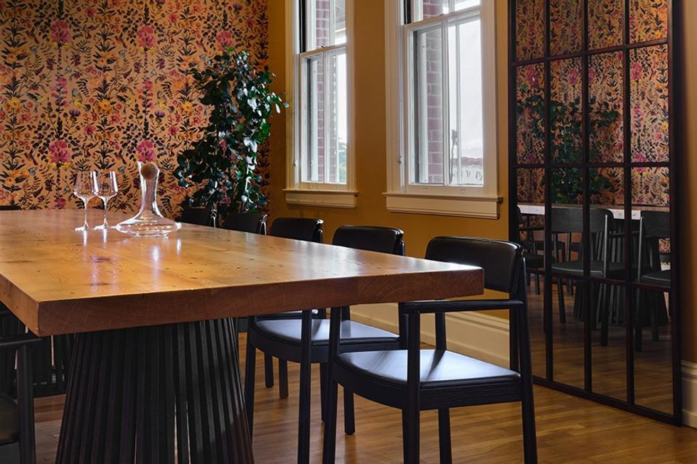 Stylish dining room with floral wallpaper, wood table, and black chairs.