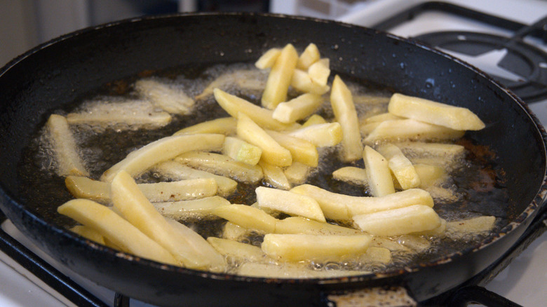 French fries cooking in a pan of frying oil.