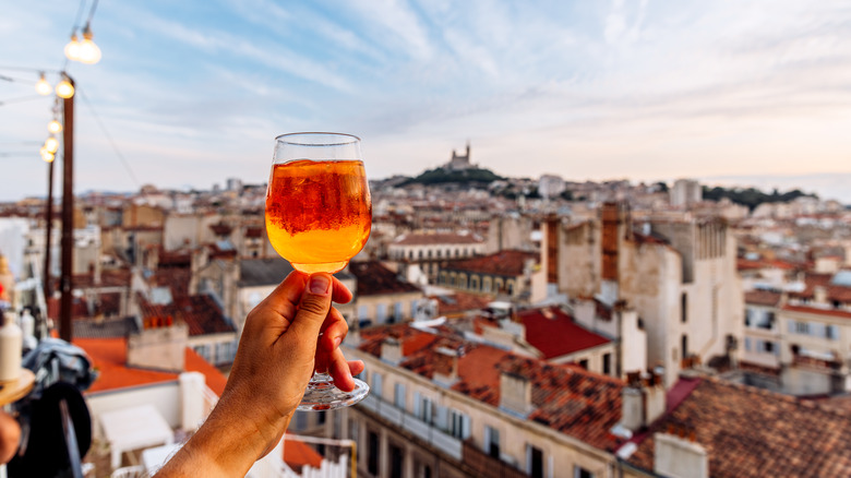 person holding Aperol Sprtiz on balcony with city backdrop