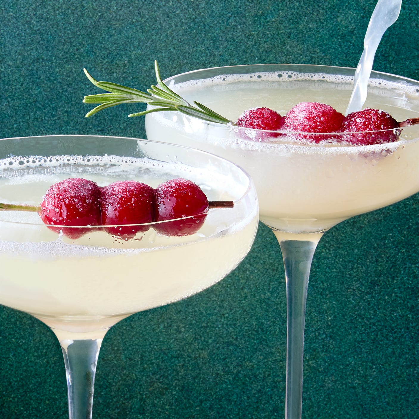 white cocktail garnished with sugared cranberries and rosemary