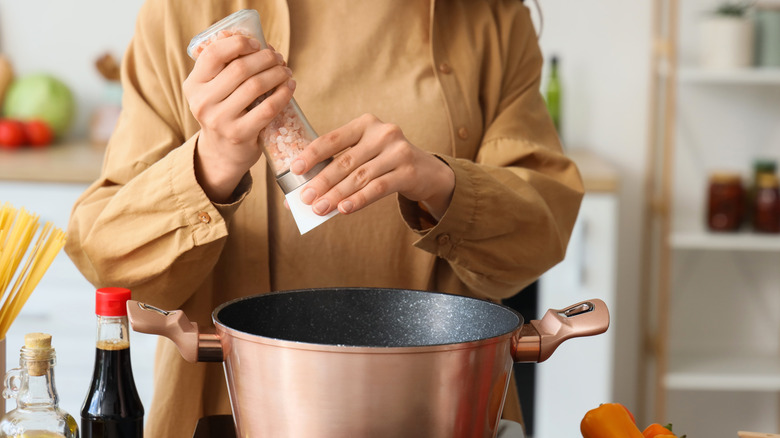 Young woman with sea salt making pasta in kitchen, closeup