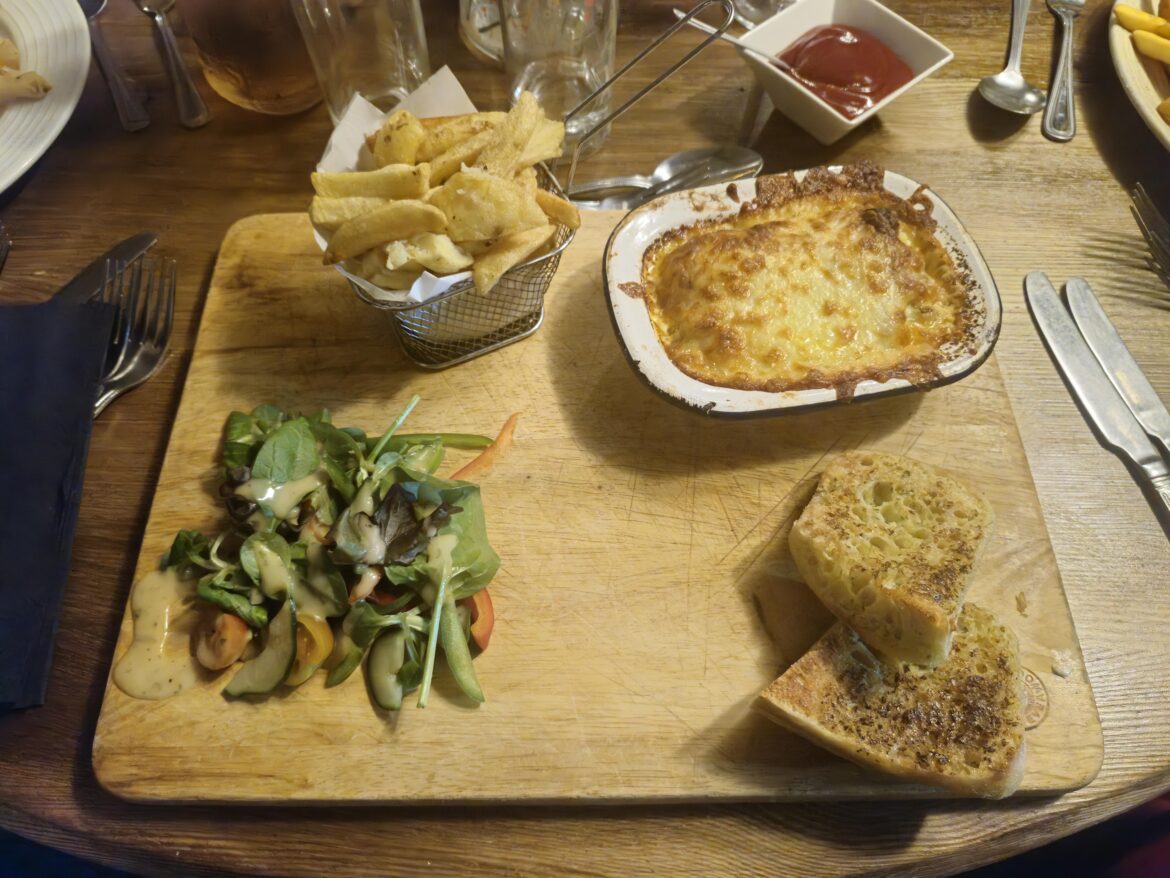 Lasagne, chips, salad and garlic bread on a chopping board