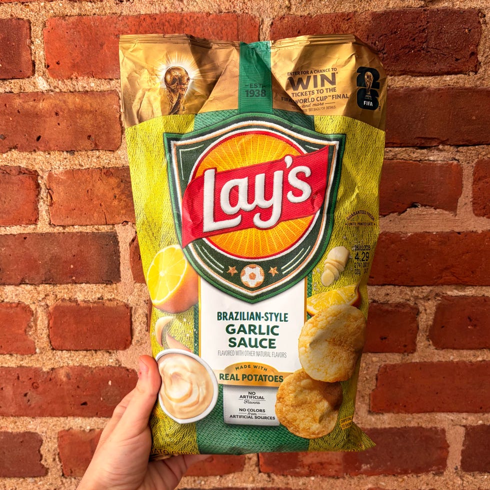 A person holding a bag of Lay's Brazilian-Style Garlic Sauce chips against a brick wall.