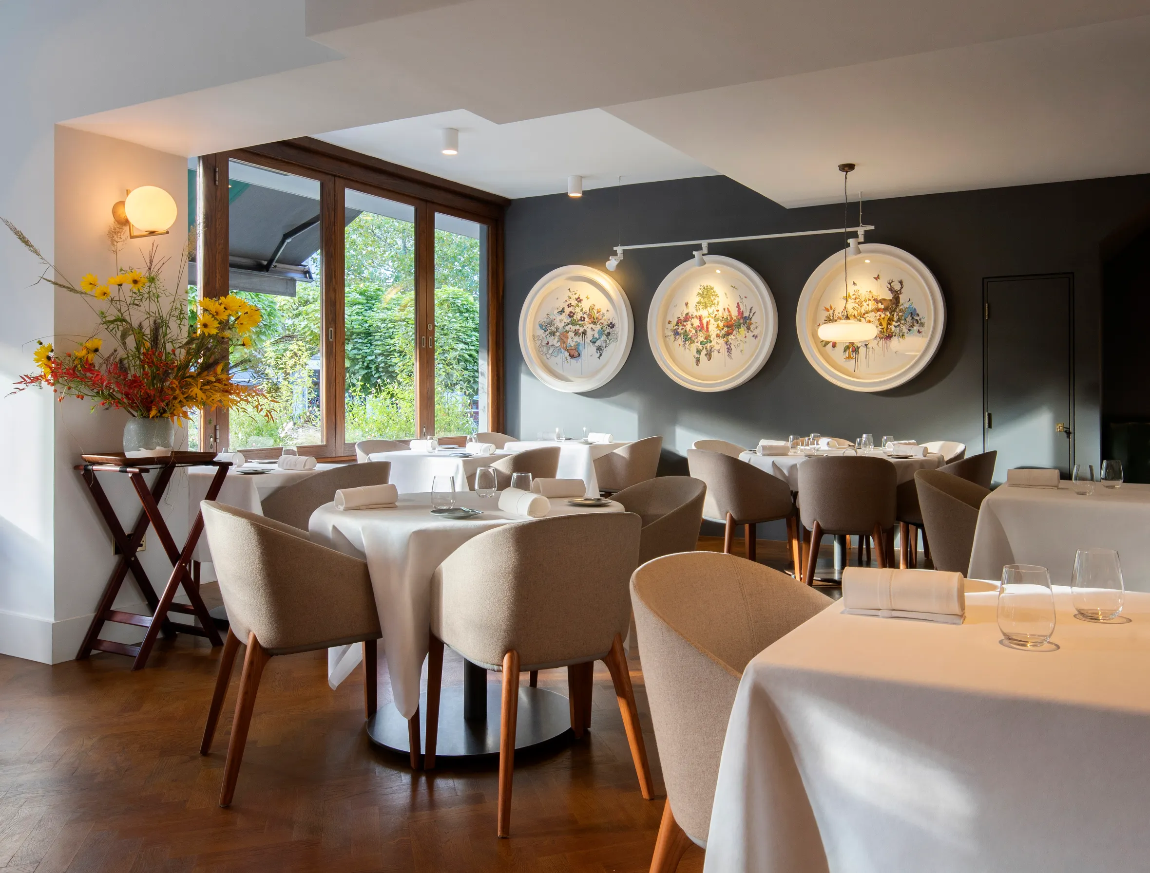Dining room with white-clothed tables, beige chairs, and circular wall art.