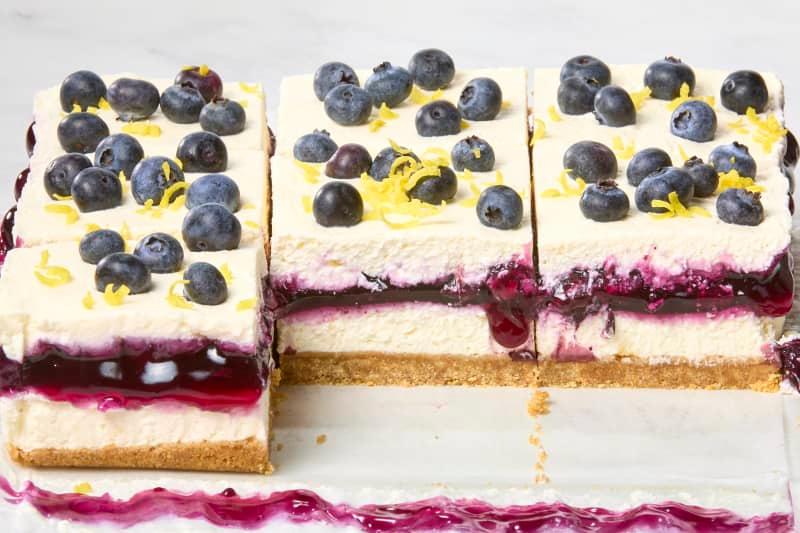 angled shot of lemon blueberry delight pieces, topped with fresh blueberries and lemon, with two missing in the front.