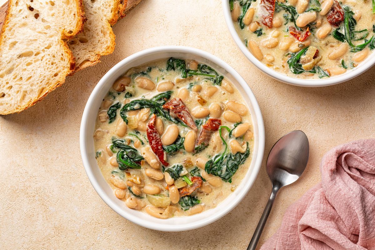 Bowls with Tuscan butter beans stew with spinach and sun-dried tomato, vegan cream. Vegetarian homemade meal.