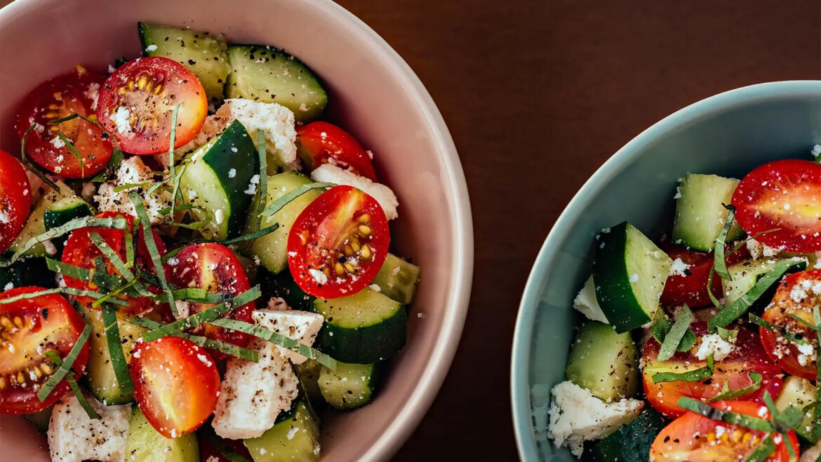 A photo of two bowls of Mediterranean Greek salad with cherry tomatoes, cucumber, feta cheese, olive oil and black pepper.