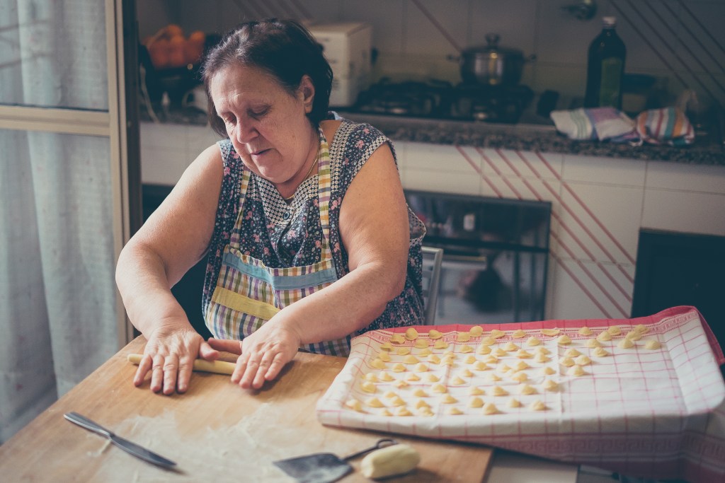 An Italian woman making homemade gnocchi on a wooden board.