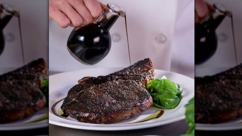 Balsamic vinegar being poured onto a ribeye steak in a white plate