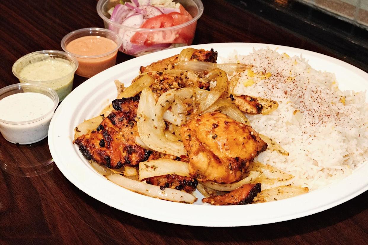 Chicken tikka with rice, onions, salad and sauces on a wood table at Bengali restaurant Roshana Bilash in Melrose Hill.