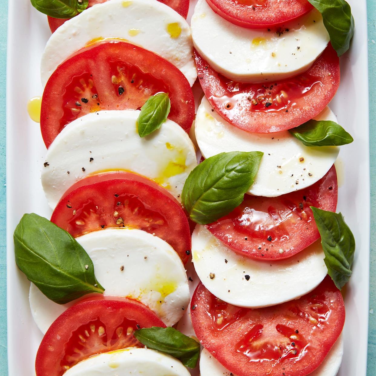 sliced tomatoes, mozzarella, and basil on a plate drizzled with olive oil