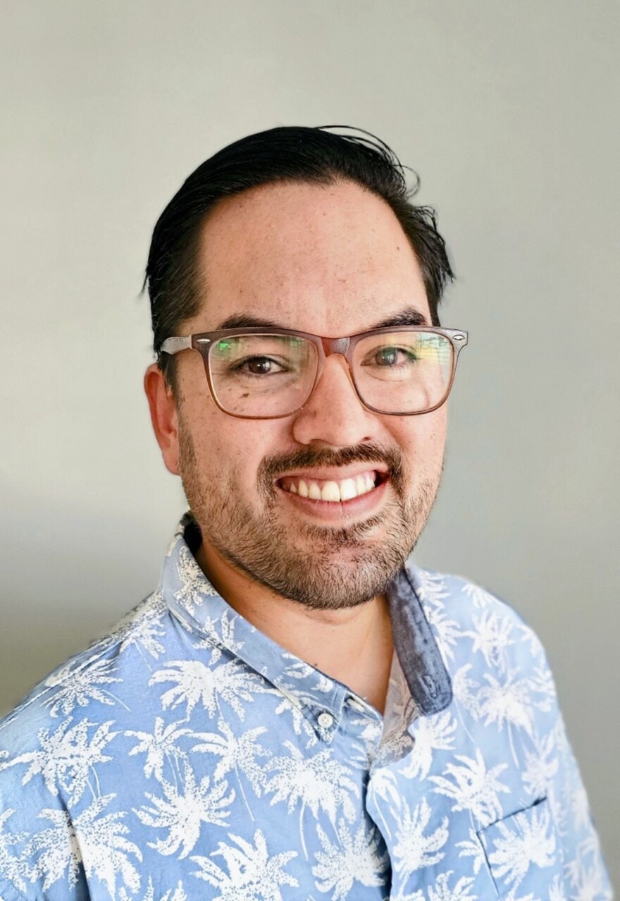 Man in blue and Hawaiian shirt and glasses smiles at camera 