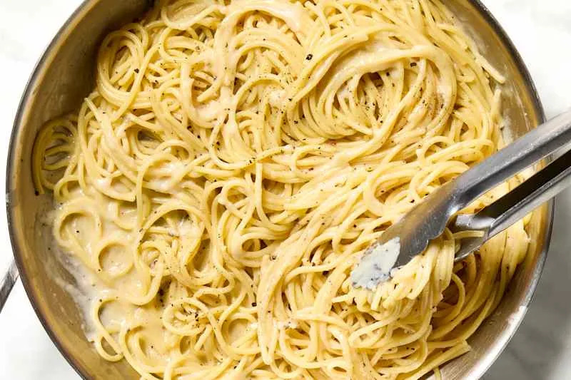 overhead shot of cacio e pepe in a pot, with tongs grabbing a serving.