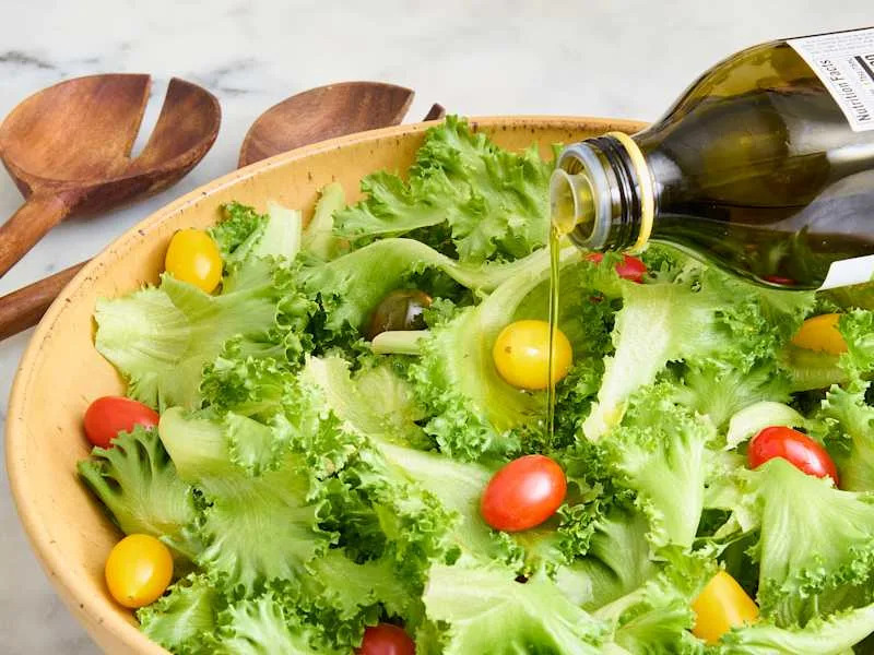 Fresh green lettuce with cherry tomatoes and yellow grape tomatoes, drizzled with olive oil in a wooden bowl.