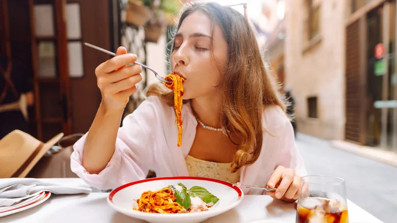 Young woman enjoying bowl of pasta outside at a cafe in what looks like a European setting.