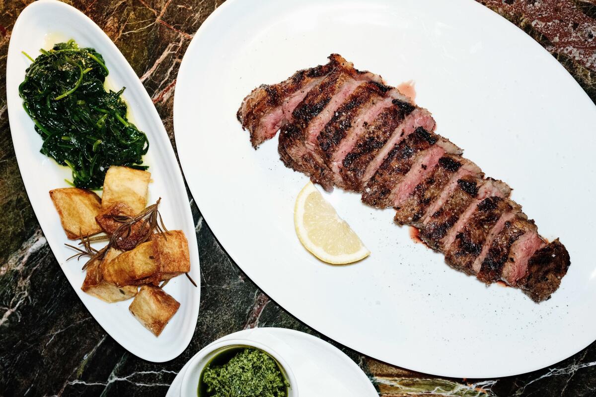 A sliced New York strip steak with spinach and potatoes on a dark marble table