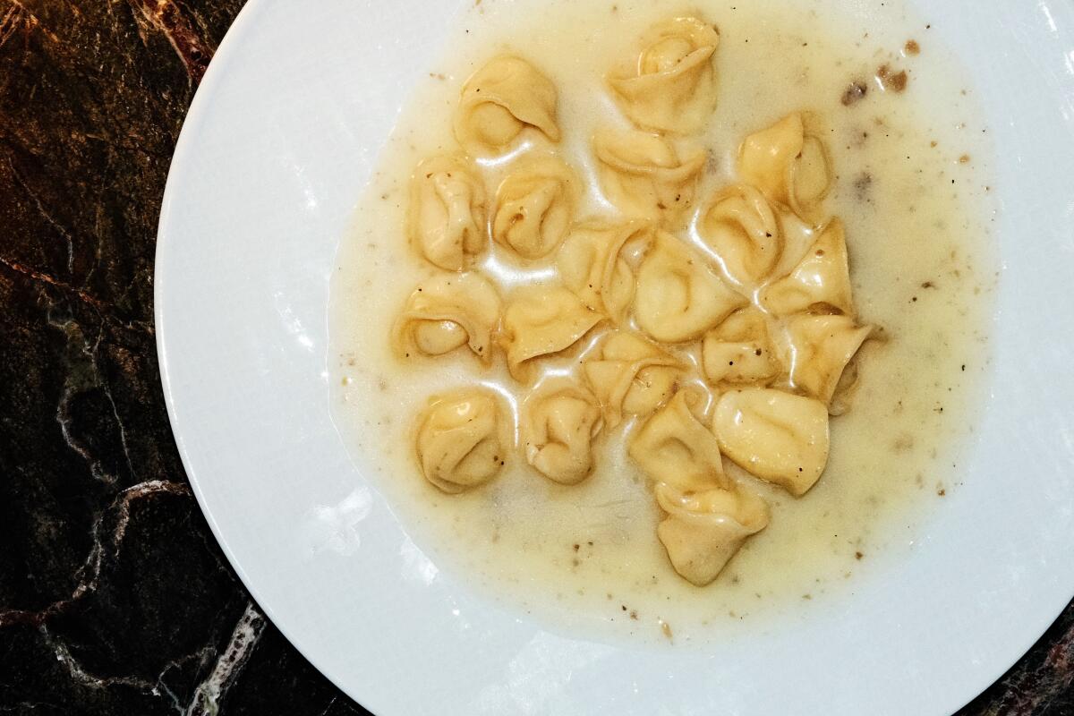 A white bowl of sweet corn tortellini on a dark marble table
