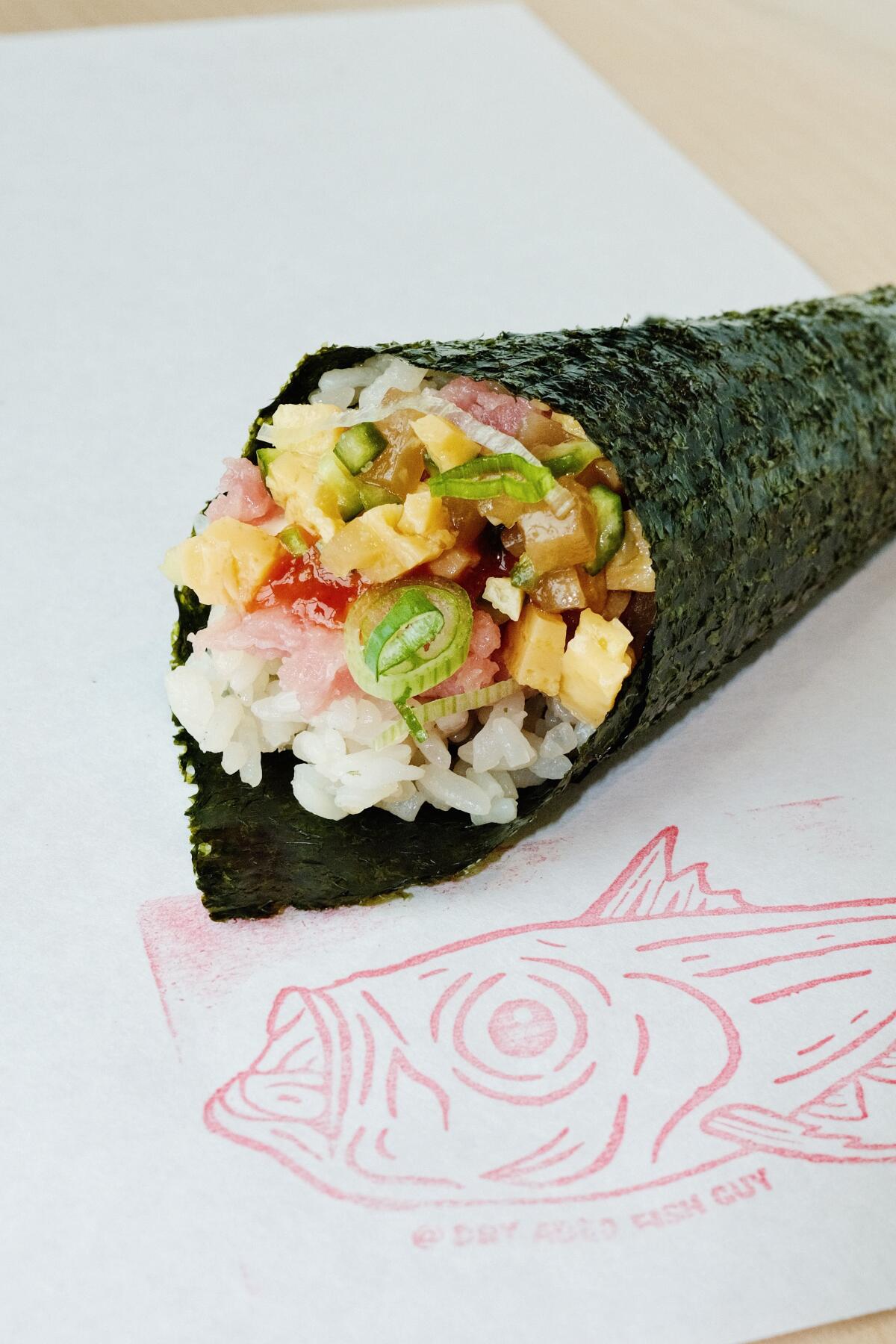 A dry-aged tuna hand roll on a white placemat stamped with a red fish