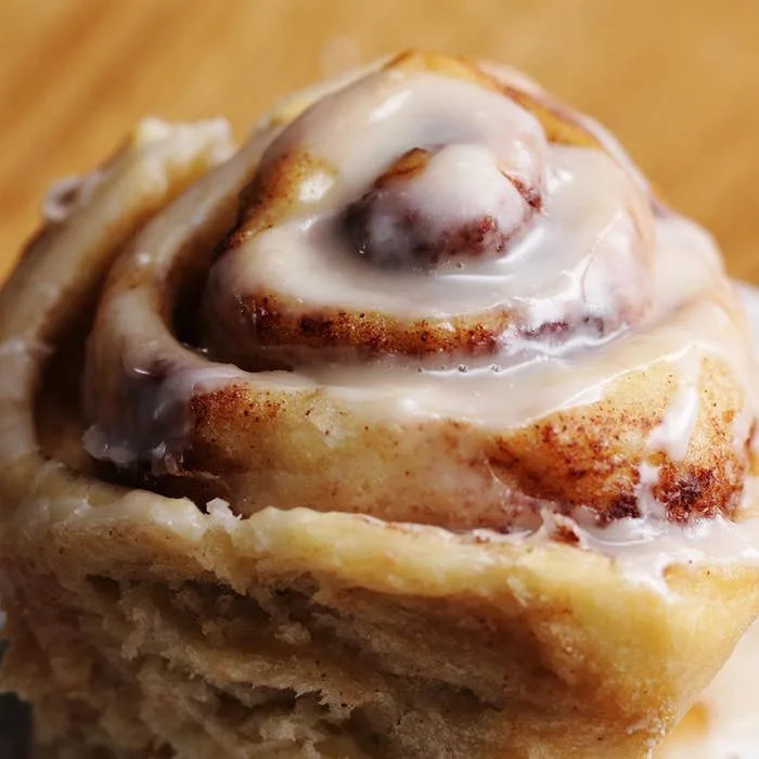 Close-up of a glazed cinnamon roll with swirled layers, topped with creamy icing