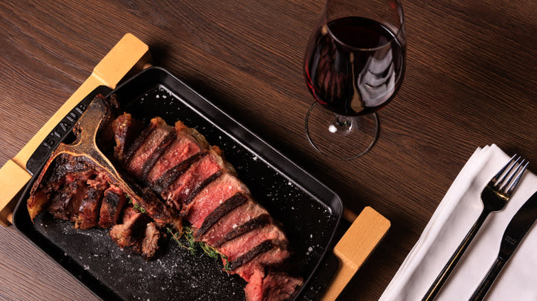 A bistecca alla fiorentina steak on a skillet with a glass of wine