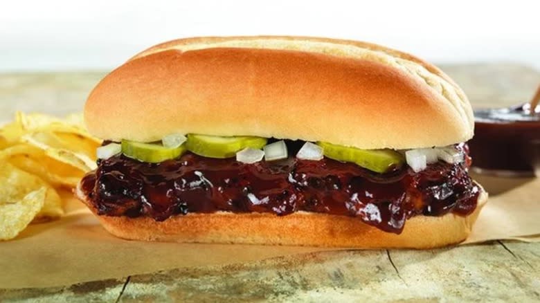 BBQ rib sandwich on an Italian roll with chips on the side