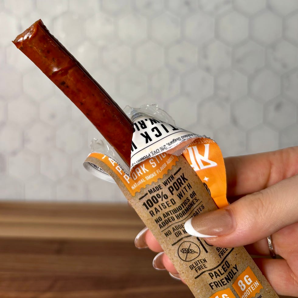 Pork stick snack partially out of its packaging held by a hand.