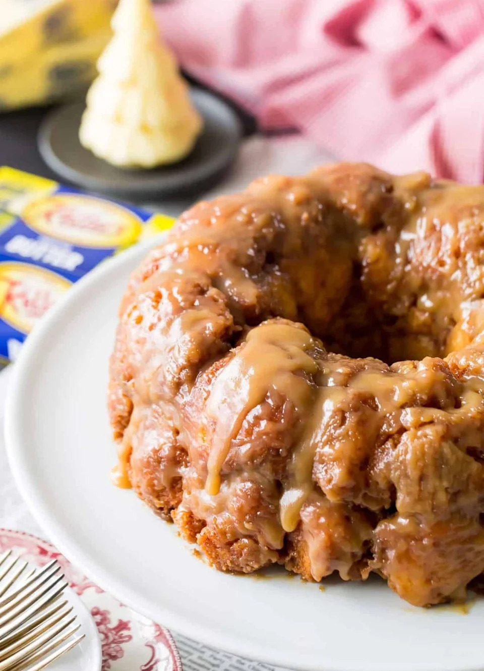 Monkey bread with caramel glaze on a white plate, with butter and baking ingredients in the background