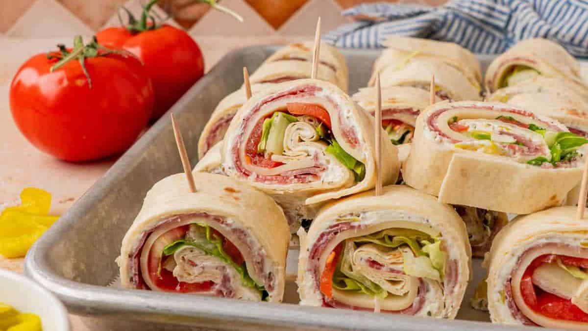 Close-up shot of a tray filled with a number of Italian pinwheels, tow whole tomatoes can be seen in the background. 