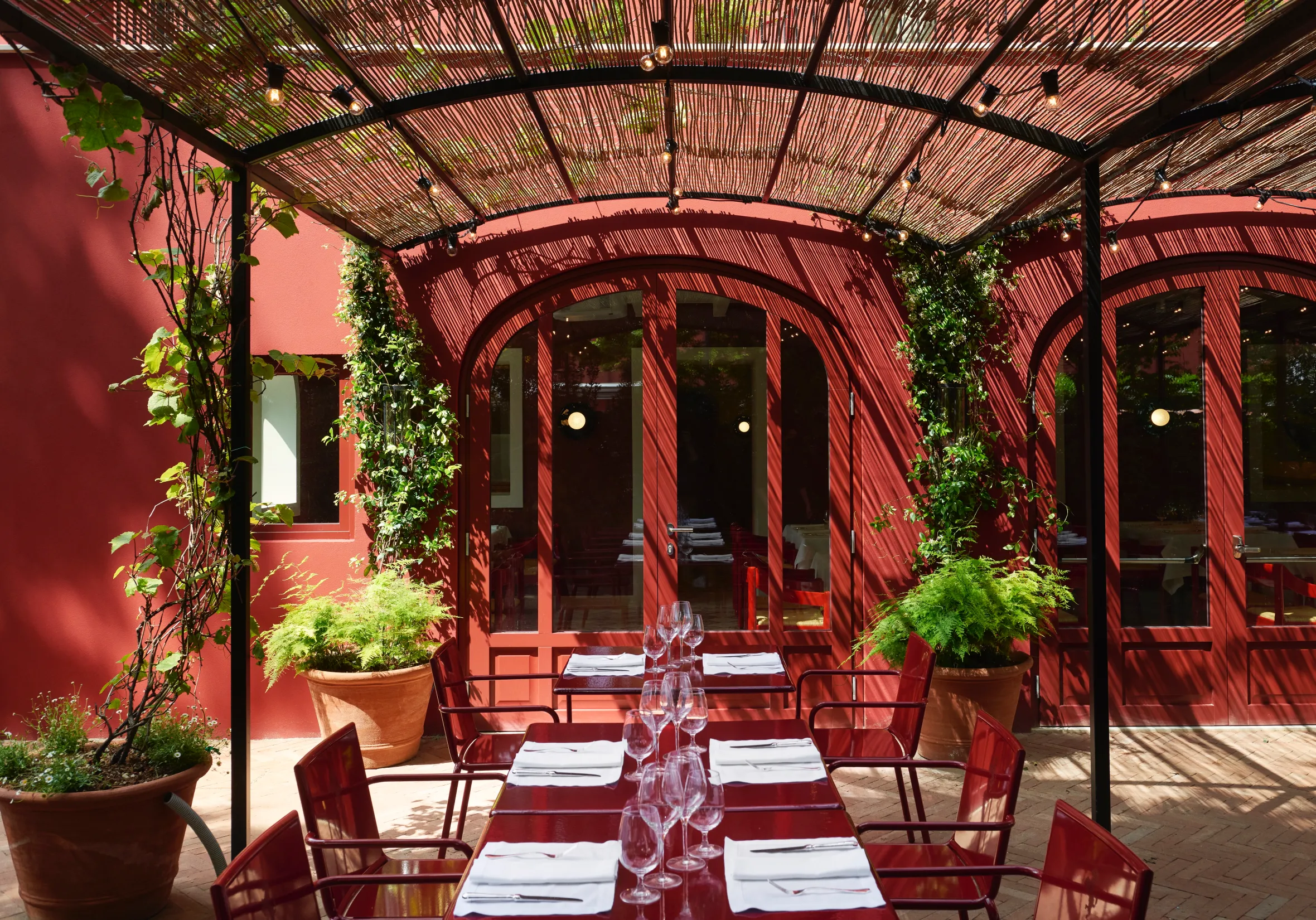 Outdoor patio dining area with red walls, red tables, and chairs, with a bamboo trellis covering.