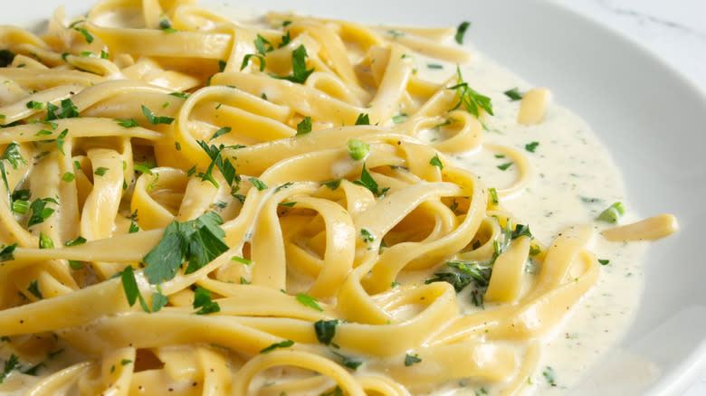 A bowl of alfredo pasta with lots of creamy sauce and parsley