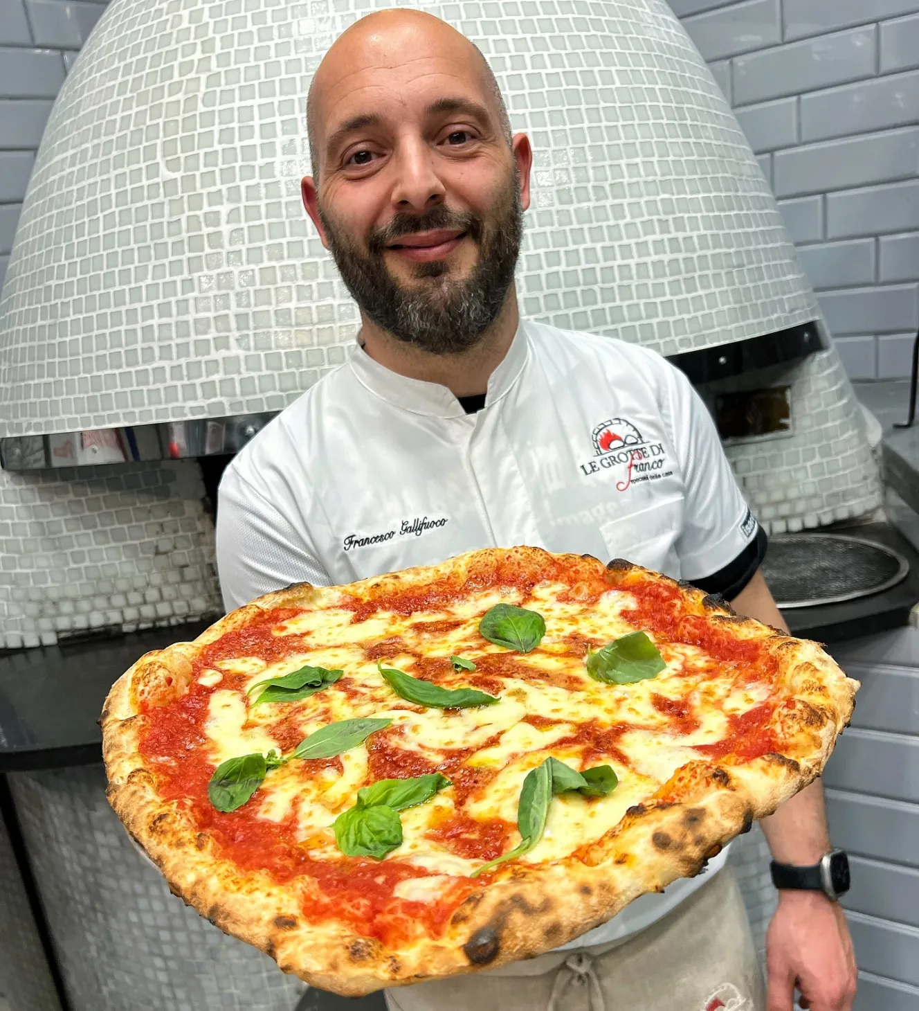 Franco Gallifuoco holding a freshly baked pizza in front of a pizza oven.