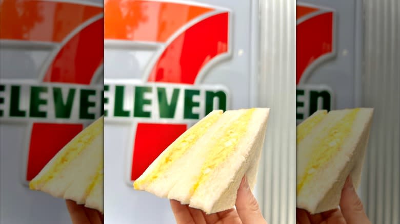 Person holding an egg sandwich with a 7-Eleven sign in the background