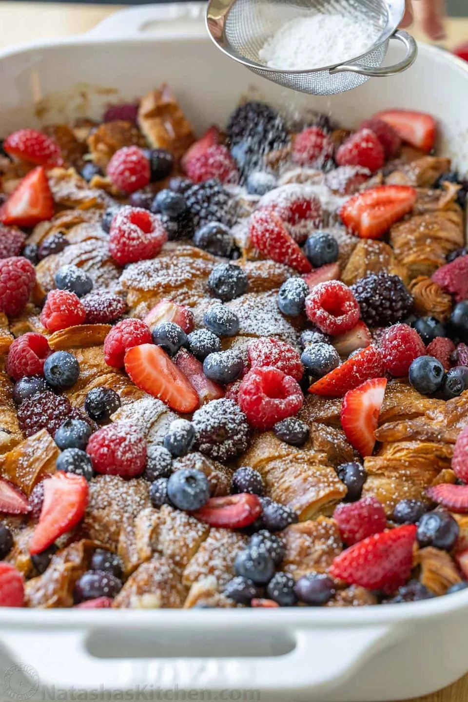 Croissant casserole topped with mixed berries and dusted with powdered sugar being prepared for serving