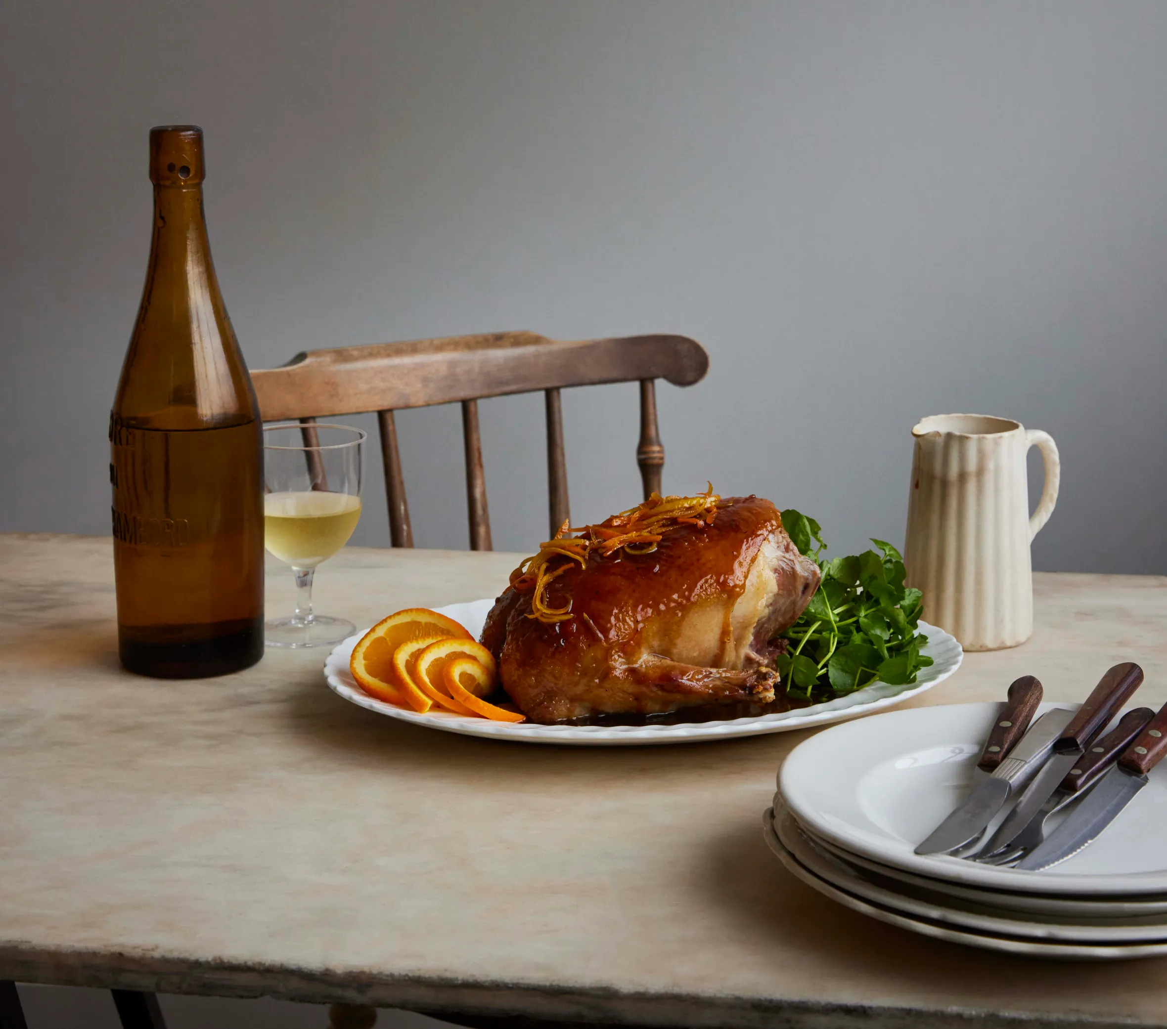 A duck a l'orange dish with orange slices, garnished with watercress, a bottle of wine, and plates with silverware on a table.