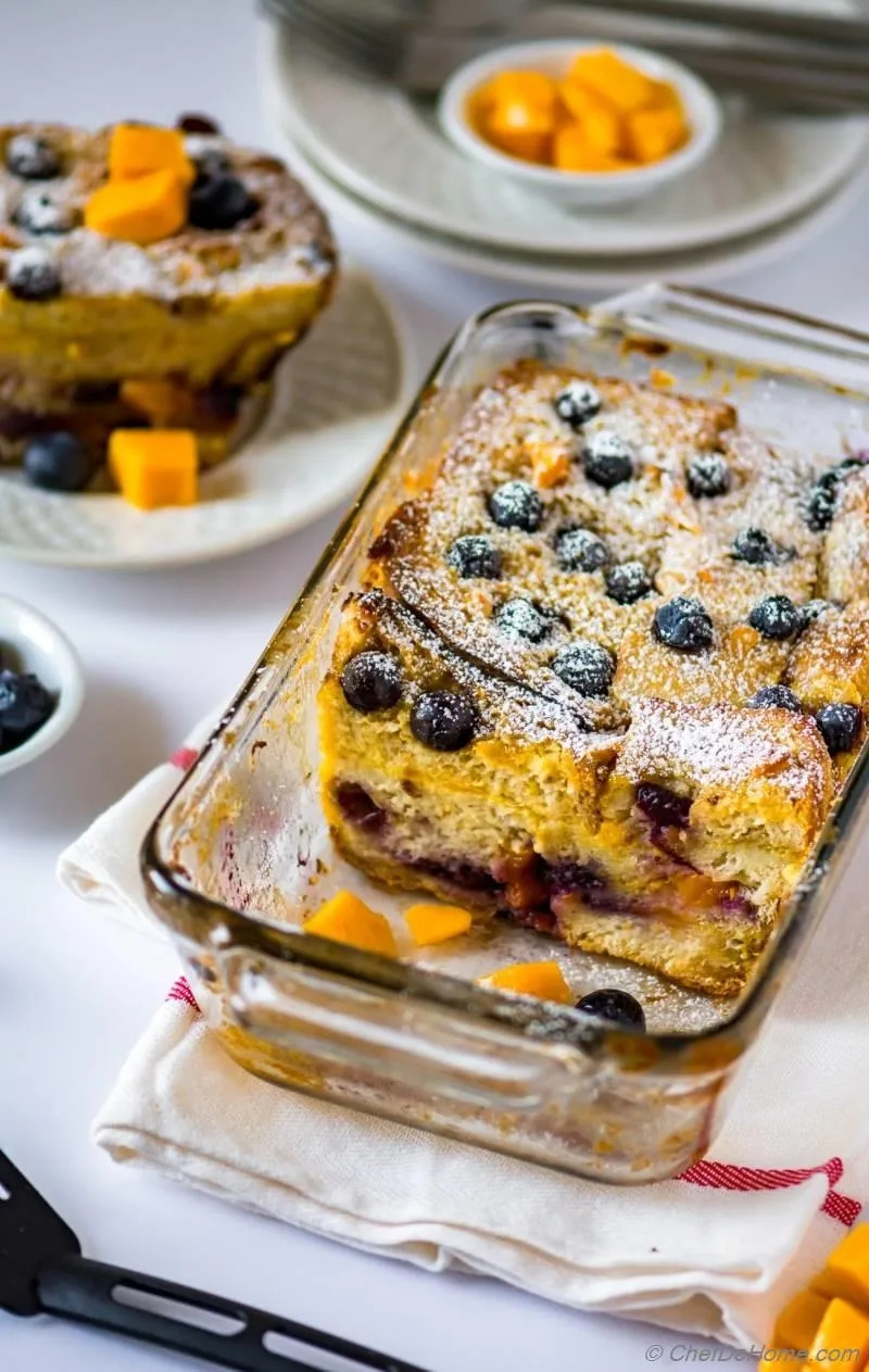 Blueberry French toast casserole topped with powdered sugar served in a glass dish, with cheese cubes on the side
