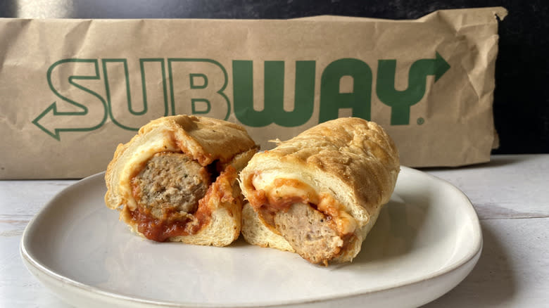 A Subway meatball sub split in half on a plate in front of the to-go packaging